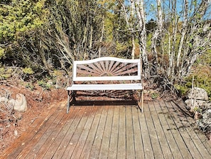A wooden bench with a sunburst design, located on a wooden deck surrounded by natural vegetation.