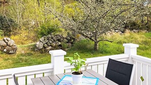A wooden deck with a table and chairs, a potted plant, and a stone wall in the background.