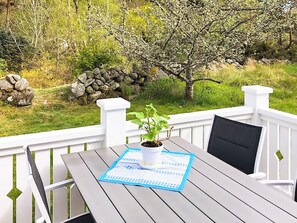 A wooden deck with a table and chairs, a potted plant, and a stone wall in the background.