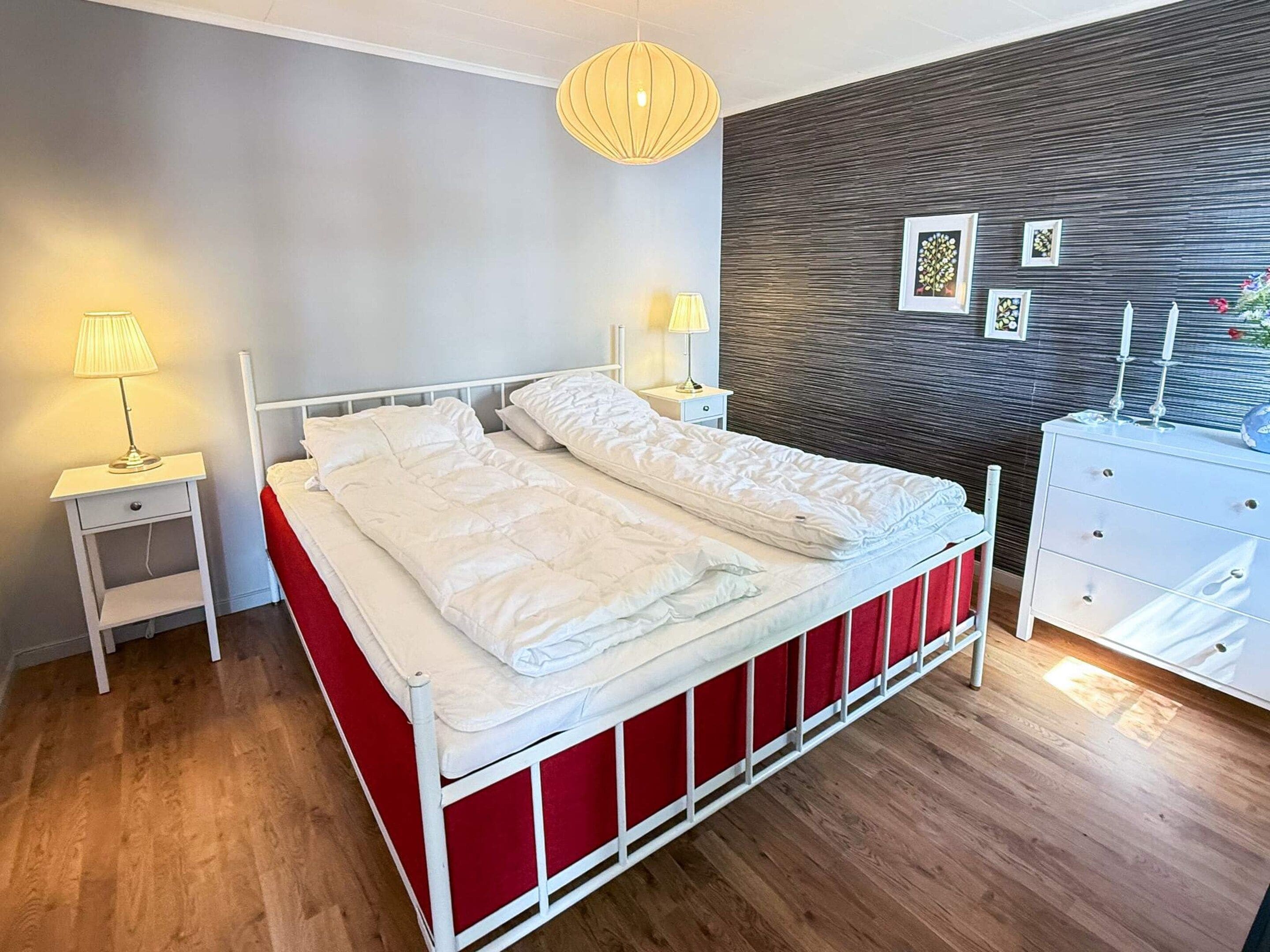 A modern bedroom with a bed, bedside lamps, a dresser, and a wall with framed pictures.