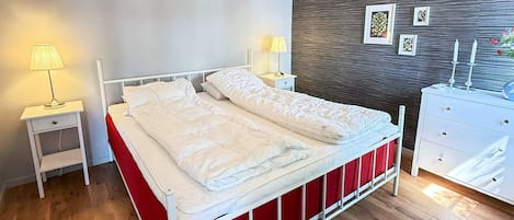 Un dormitorio moderno con cama, lámparas de noche, cómoda y una pared con cuadros.