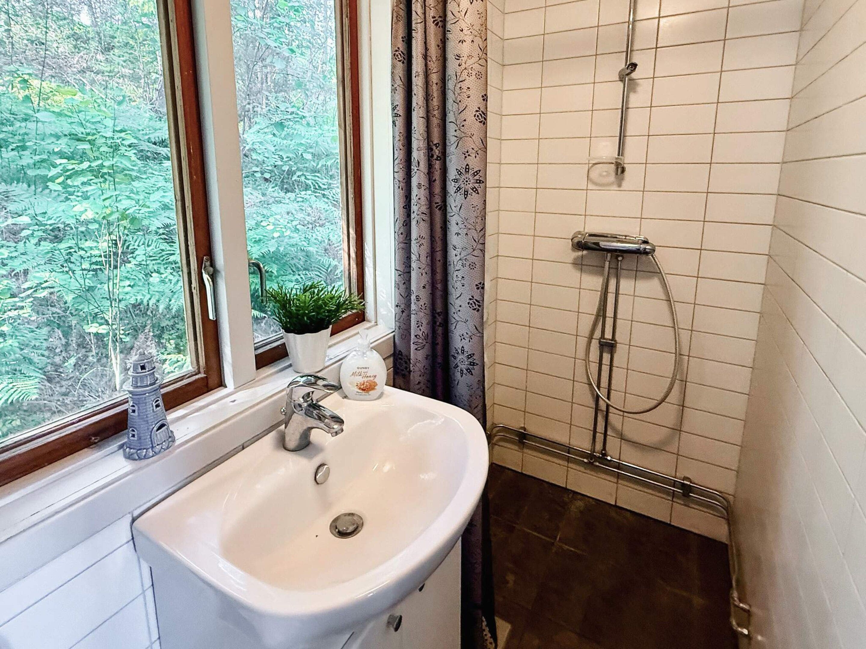 A bathroom with a sink, a window with a view of greenery, a shower, and a potted plant.