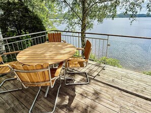 A wooden deck with a round table and chairs, overlooking a body of water.
