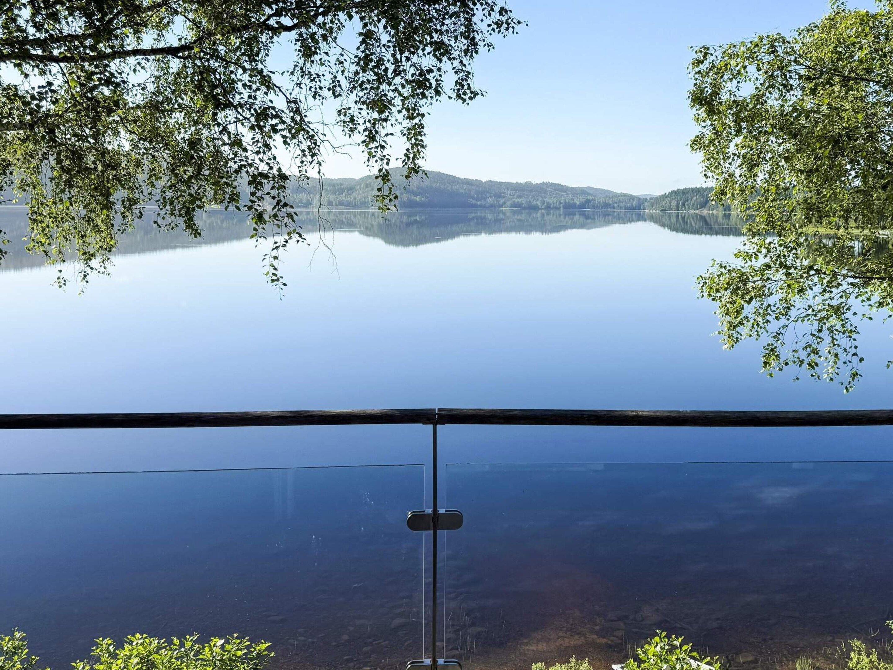 Vista clara de um lago, com uma cadeia montanhosa distante emoldurada por árvores.