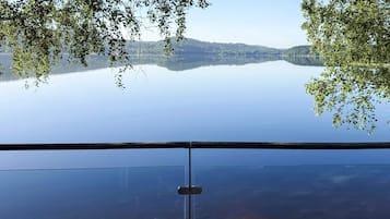 Vista clara de um lago, com uma cadeia montanhosa distante emoldurada por árvores.