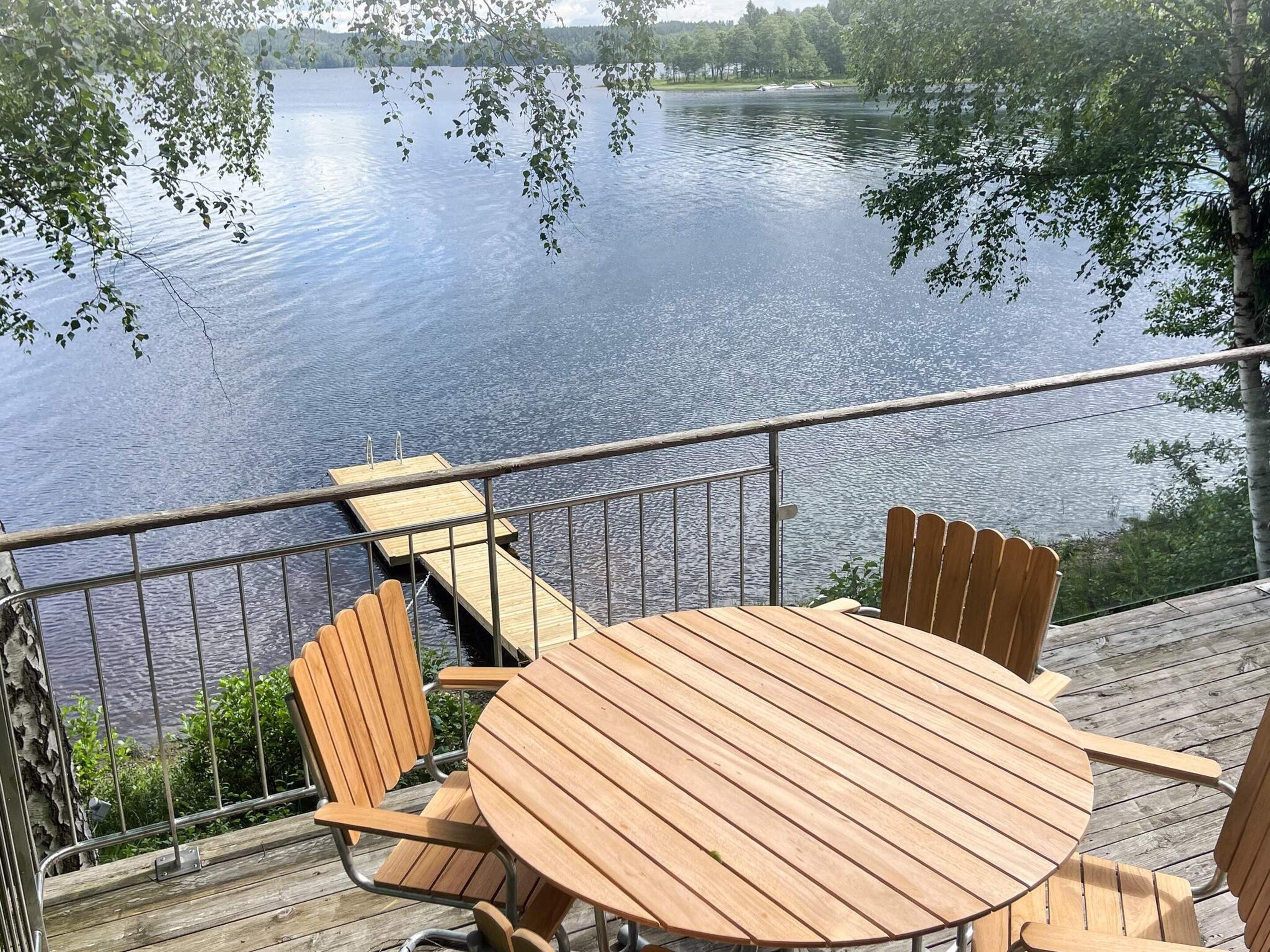 A wooden deck with a round table and chairs overlooking a calm lake.