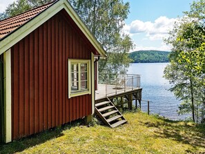 A red cabin with a wooden deck and a window, overlooking a lake. - 4 Person Holiday Home in Bullaren (Bullaren)