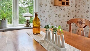 Een eettafel met bloemenbehang, een houten kast en een raam met uitzicht op bomen.