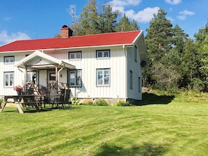 A two-story white house with a red roof, a porch with outdoor furniture, and a well-maintained lawn.