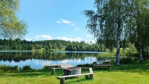 Een picknickplaats aan het meer met houten banken en picknicktafels, omgeven door weelderige begroeiing en een helderblauwe lucht.