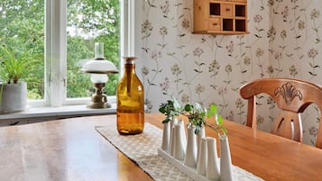 Uma mesa de jantar com um jogo de mesa de renda, um vaso com plantas e um armário de madeira com papel de parede floral.