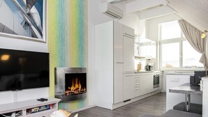 A modern living room with a flat-screen TV, a fireplace, and a kitchen in the background. - Holiday Home in Wendtorf (Wendtorf)