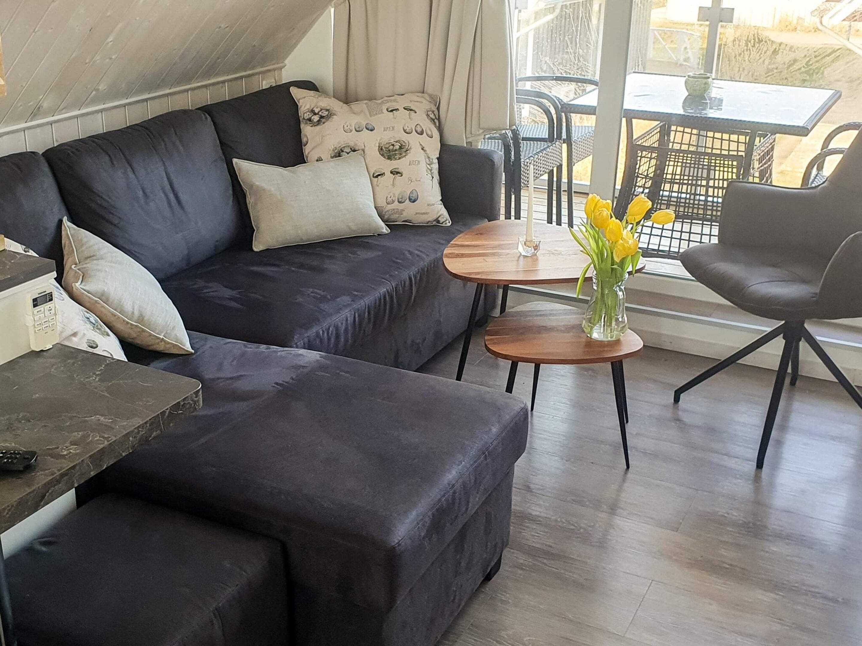 A modern living room with a dark-colored sofa, a small round table with a vase of flowers, and a chair.