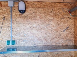 Una habitación con piso de madera, estructura de cama de metal y una lámpara fijada a la pared.