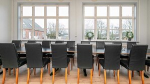 A conference room with large windows, black chairs with wooden legs, and a wooden floor.