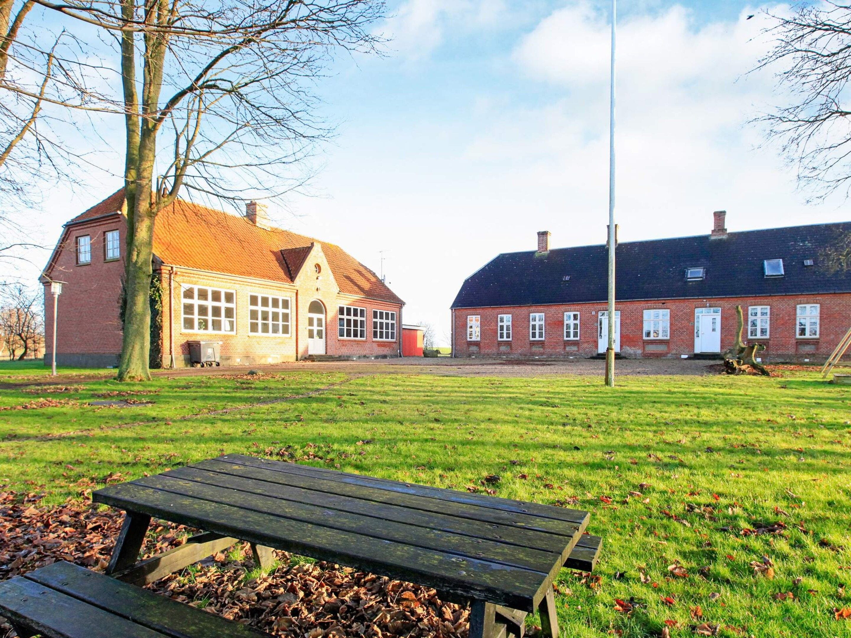 A park with a picnic table, a brick building with a red roof, and another brick building with a dark roof.