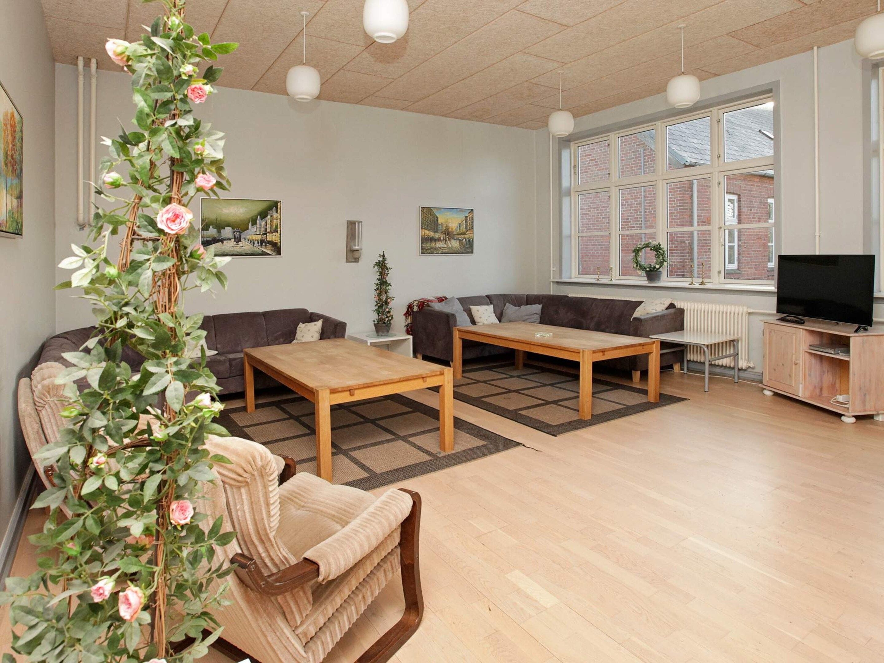 A living room with a sofa, two wooden tables, a TV stand, and a large window with a view of a brick building.