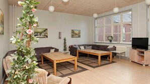 A living room with a sofa, two wooden tables, a TV, and a large window with a view of a brick building.