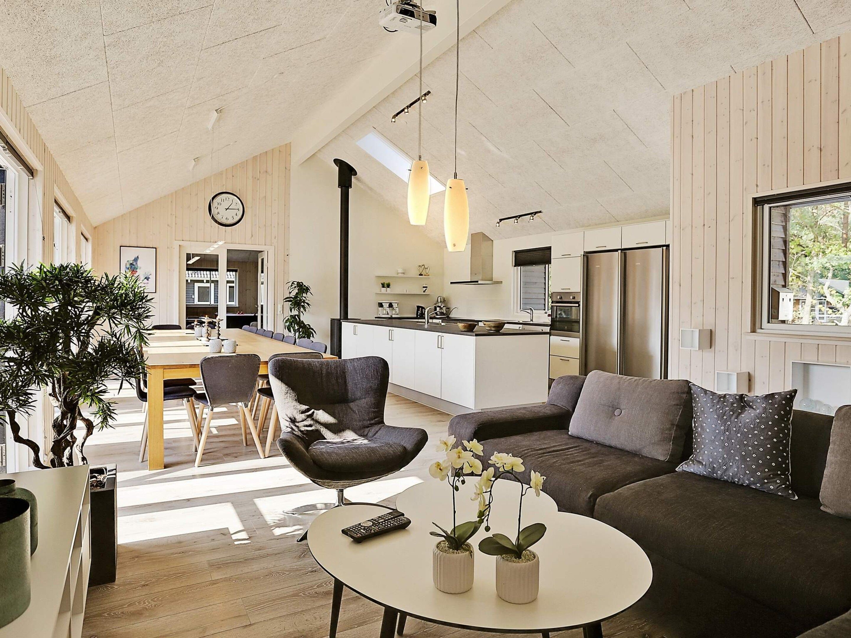 A spacious living area with a sofa, a round coffee table, and a dining table with chairs. There is a kitchen area with modern appliances and a large window.