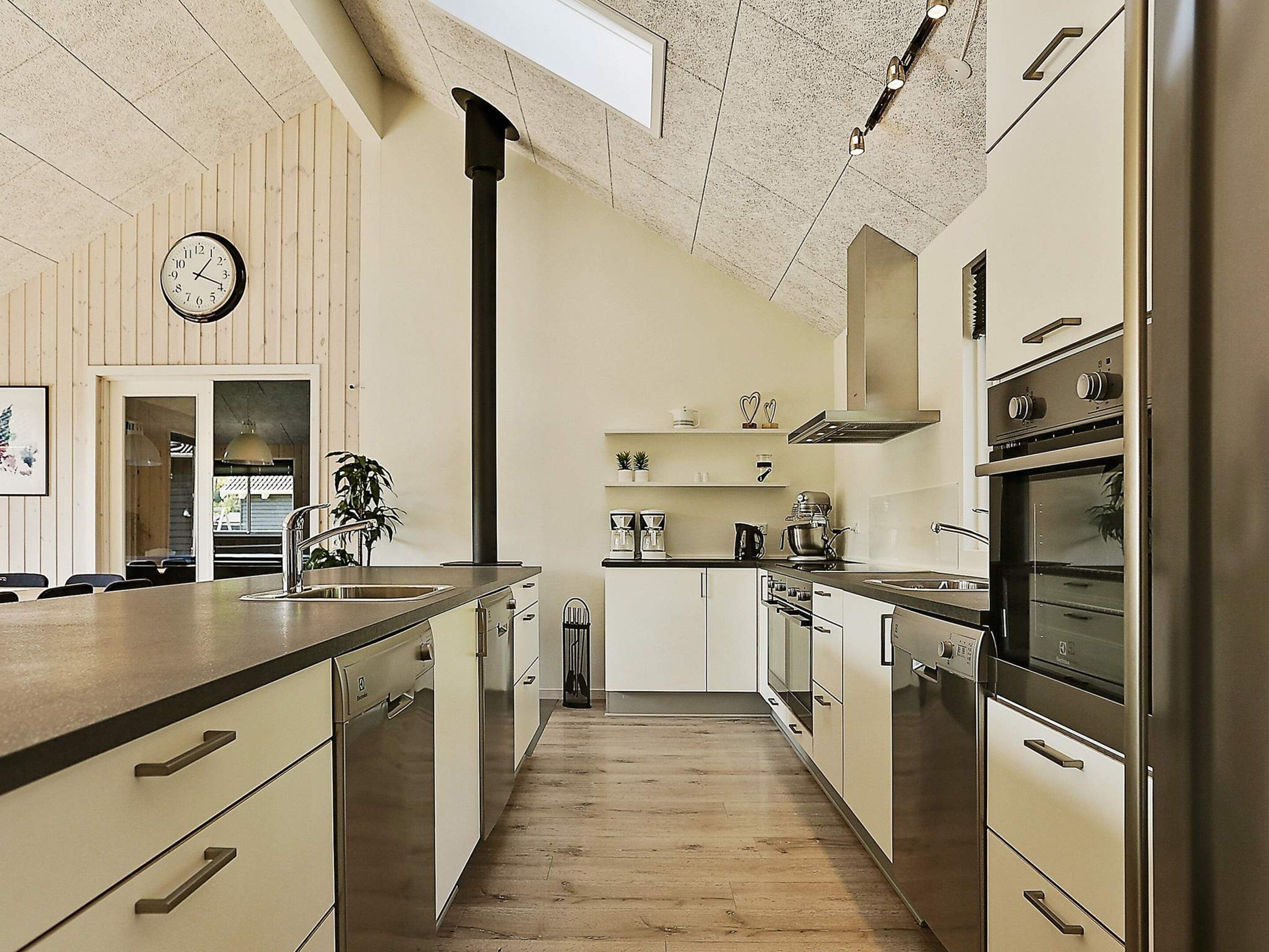 A modern kitchen with wooden flooring, stainless steel appliances, and a visible clock on the wall.