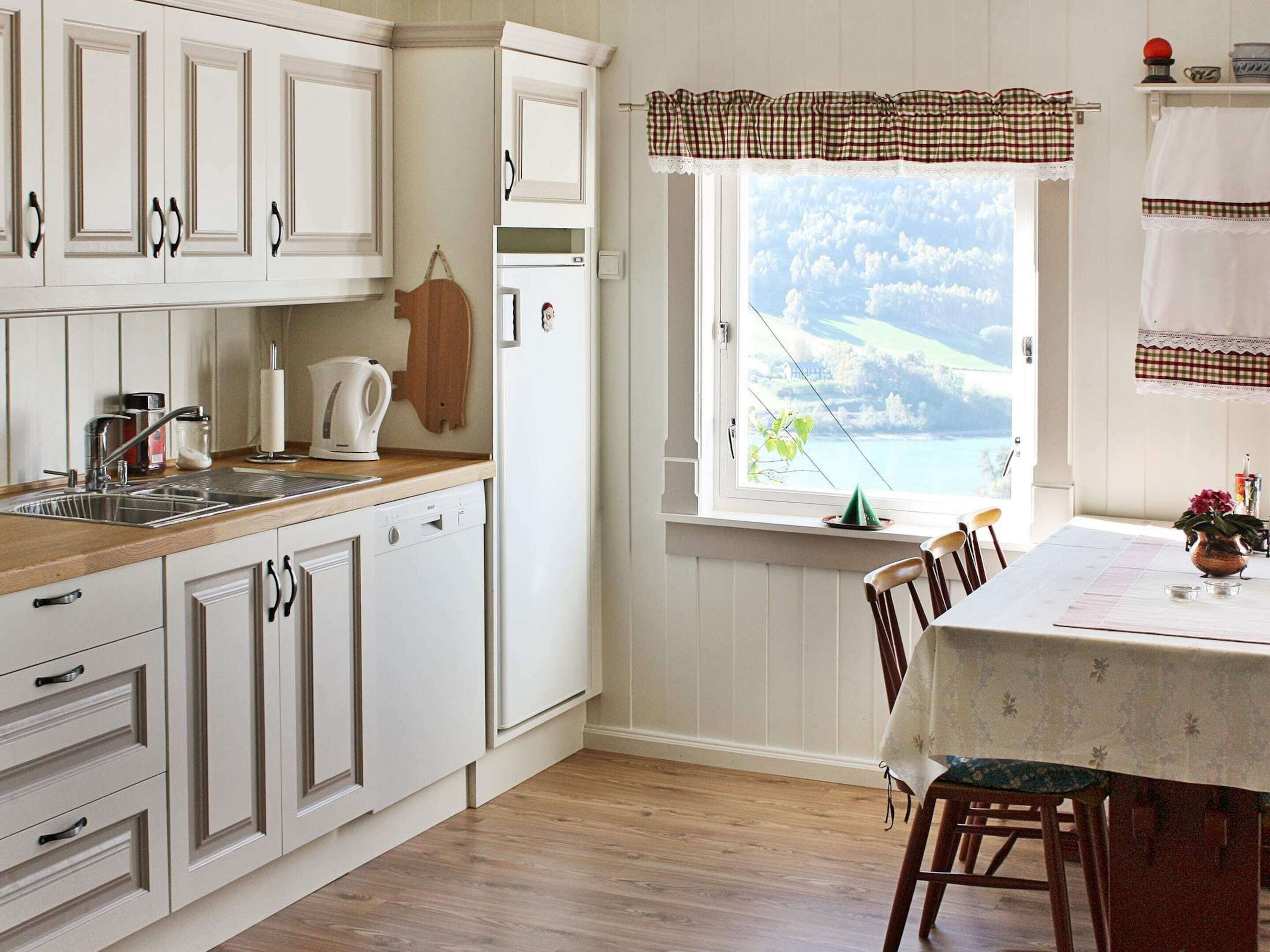 A kitchen with white cabinets, a wooden countertop, a window with a view, and a dining area with a table and chairs.