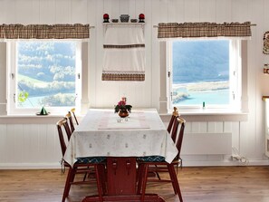 A dining area with a table set for four, two windows with curtains, and a view of a landscape.