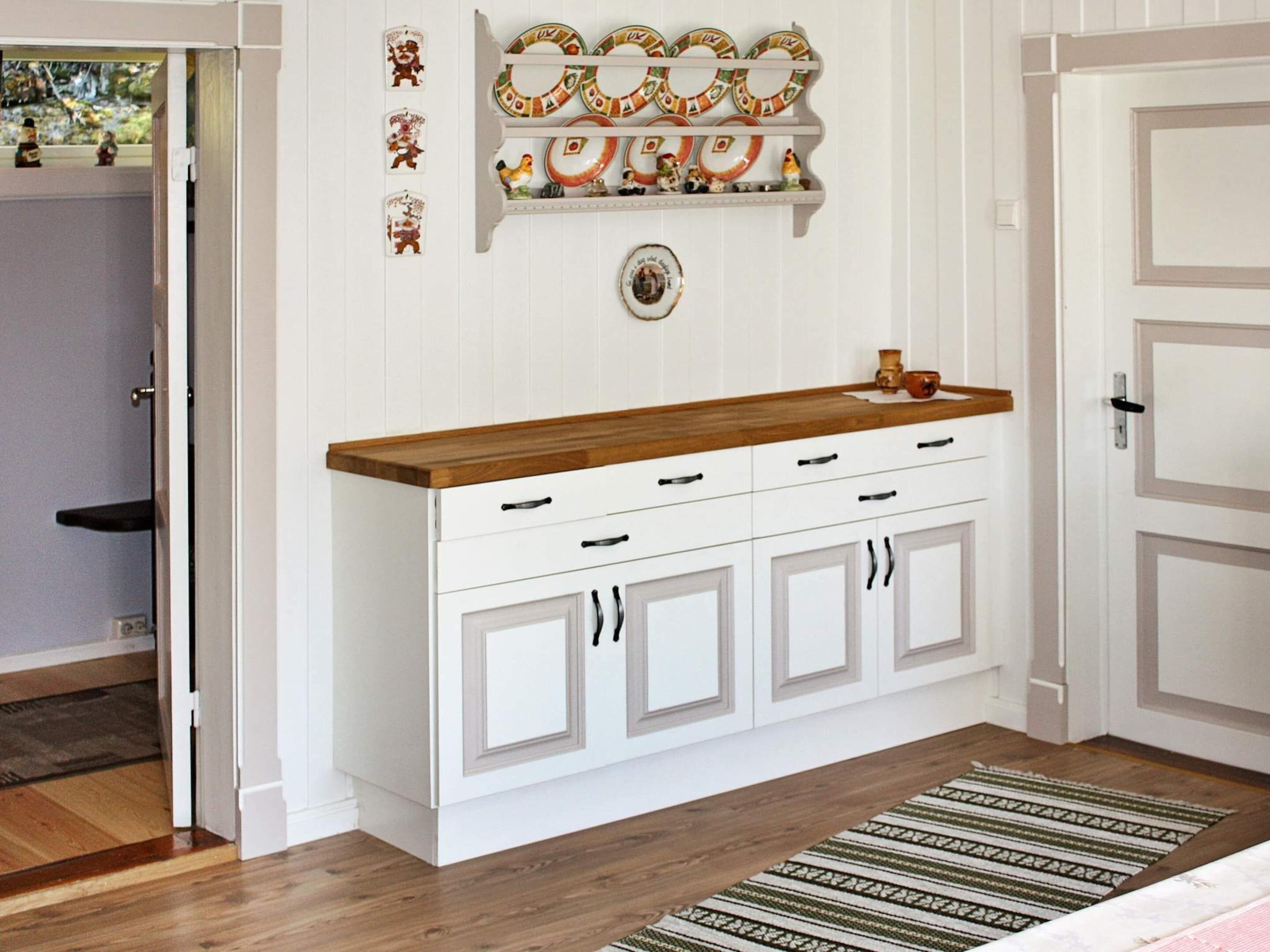 Cucina con mobili bianchi, piano di lavoro in legno ed una mensola decorativa per piatti.