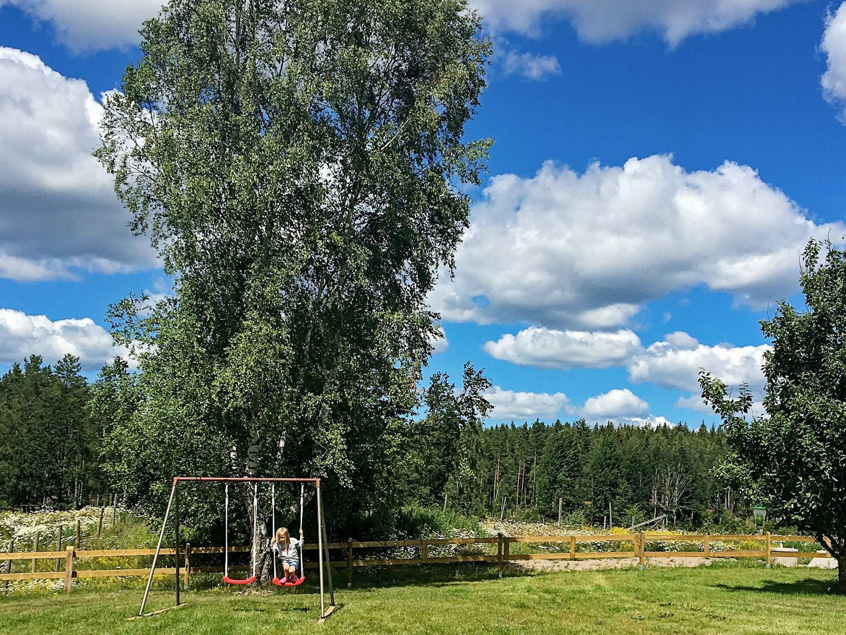 A swing set in a grassy area with trees and a clear sky.