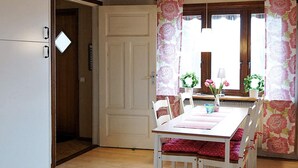 Un coin repas avec une table et des chaises blanches, un plancher en bois et une porte donnant sur une autre pièce.