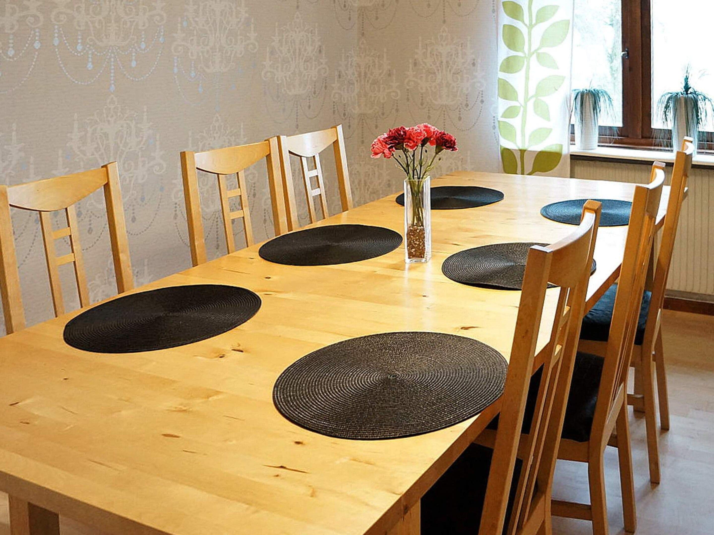 A wooden dining table with black placemats, surrounded by wooden chairs.