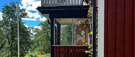 A two-story building with a balcony, a wooden fence, and a view of greenery.