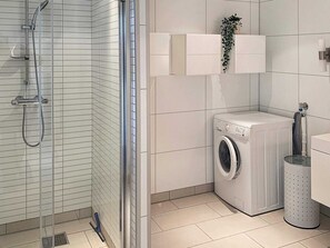Un baño moderno con ducha de vidrio, lavadora de carga frontal y una pequeña estantería con una planta.
