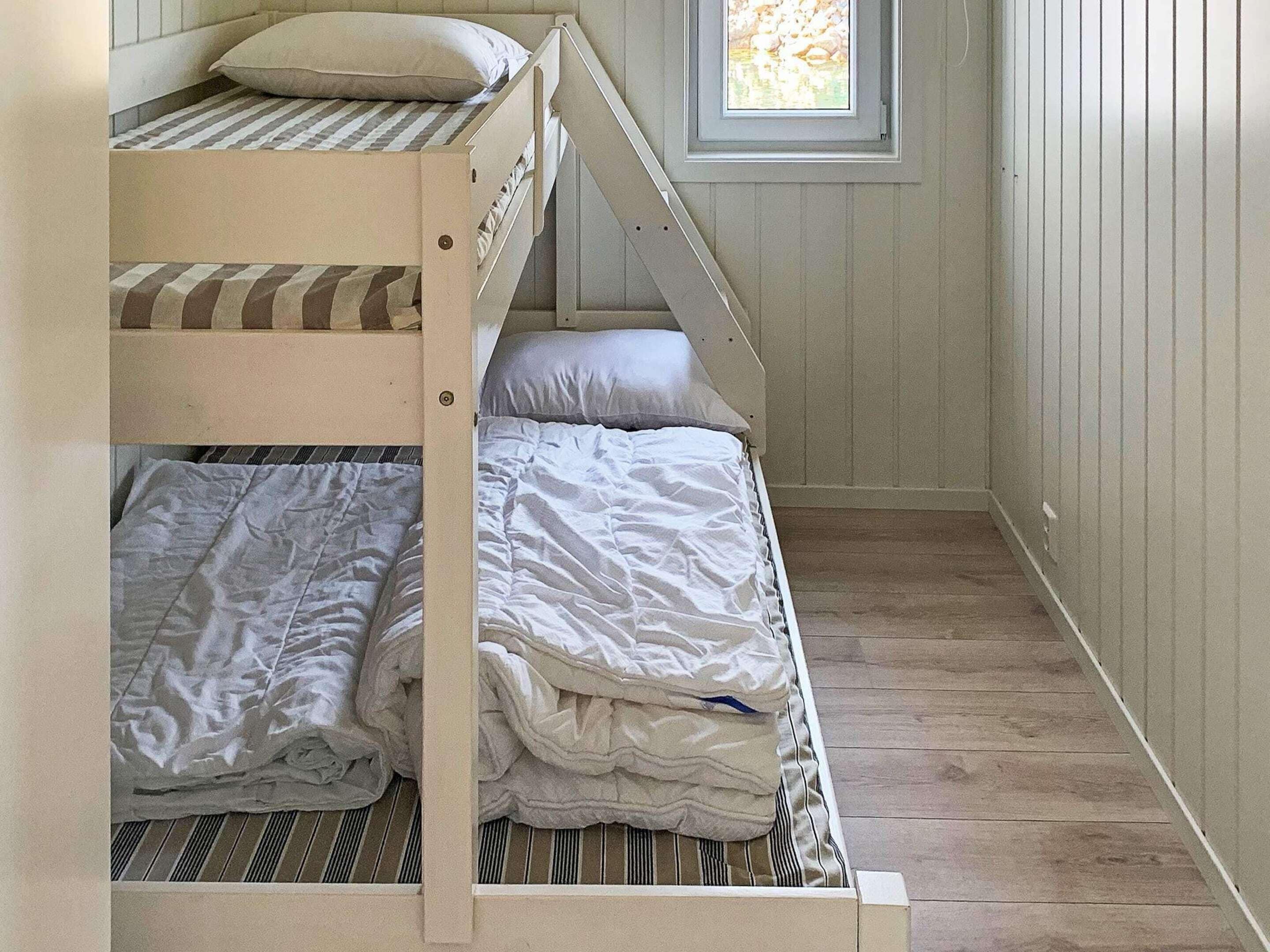Dormitorio con literas, ventana y suelo de madera.