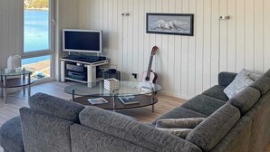 Una sala de estar moderna con un sofá gris, una mesa de centro de vidrio, un televisor y una guitarra.