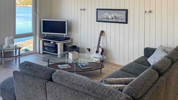 Uma sala de estar moderna com um sofá cinza, uma mesa de centro de vidro, uma televisão e uma guitarra.