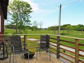 A wooden deck with two chairs and a flower pot, overlooking a grassy field and trees. - 5 Person Holiday Home in Varekil (Varekil)
