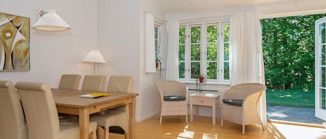 A dining area with a wooden table and chairs, a lamp, and a window with curtains.