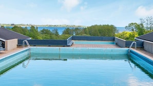 A swimming pool with clear blue water, surrounded by a concrete deck, and overlooking a body of water with trees in the background. - 4 Star Holiday Home in Aabenraa (Aabenraa)