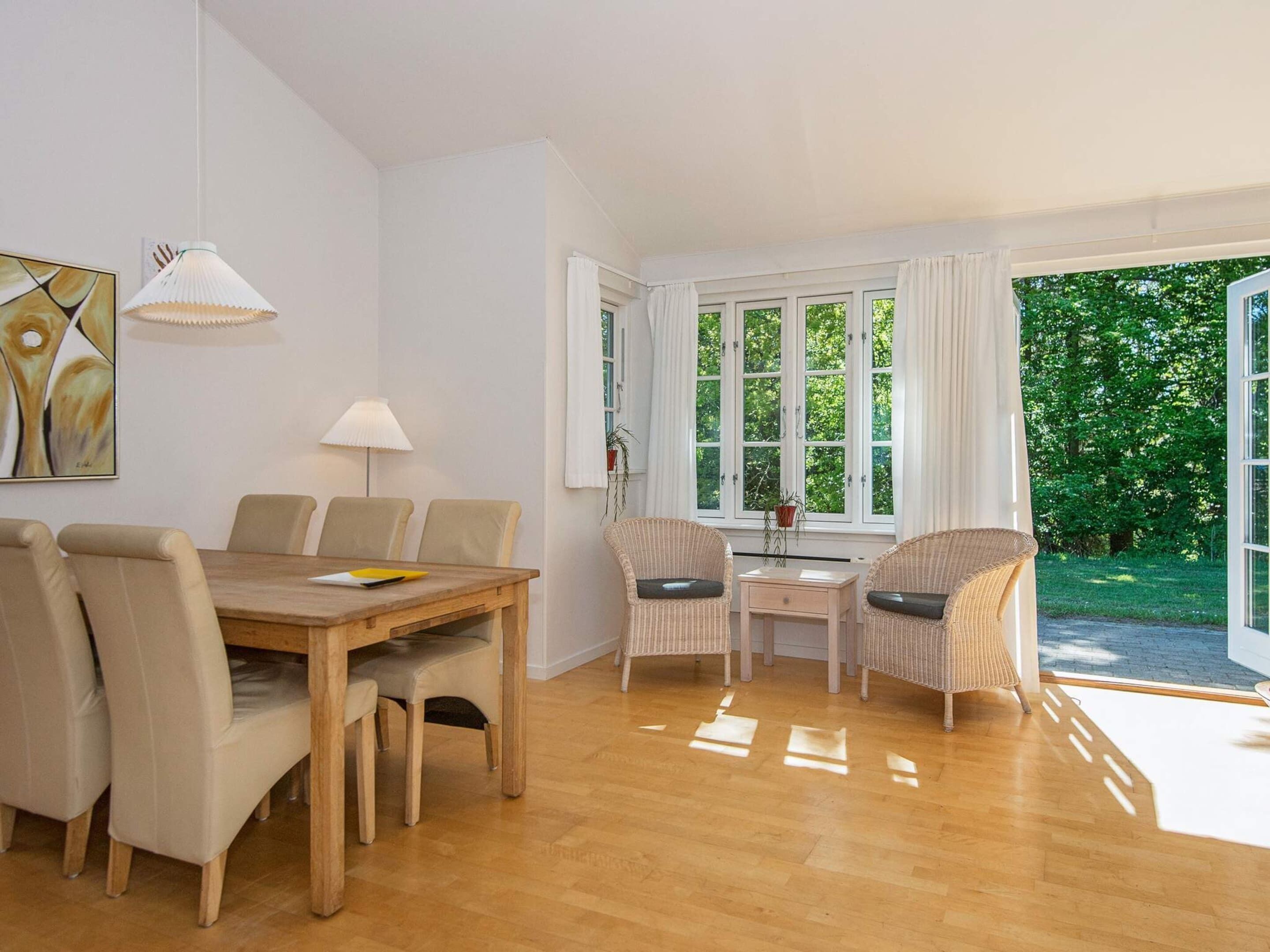 Uma sala de jantar com mesa e cadeiras de madeira, uma luminária e uma janela com cortinas.