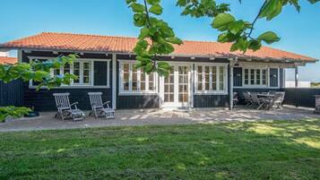 Uma casa com telhado de telhas vermelhas, varanda coberta com móveis de exterior e um gramado.