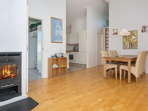 A modern living room with a fireplace, a dining area with chairs, and a kitchen in the background.
