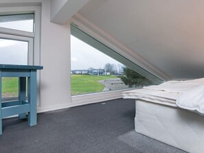 Una habitación con techo inclinado, una ventana, una mesita y una cama.