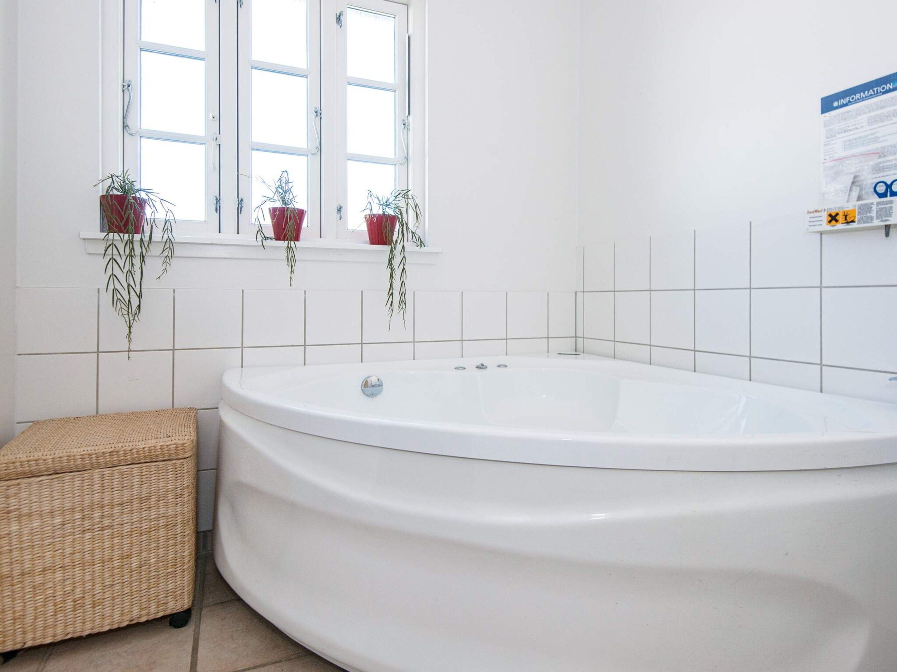 Un baño con una bañera independiente, un taburete de mimbre y plantas en macetas en el alféizar.