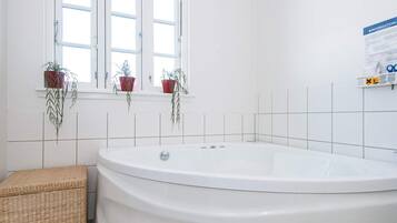 Un baño con una bañera independiente, un taburete de mimbre y plantas en macetas en el alféizar.