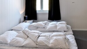 Un lit bien fait, avec du linge de lit blanc, dans une pièce dotée d’une fenêtre et d’une table de chevet.