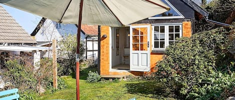 A house with a garden, a patio with a table and chairs, and a large umbrella.
