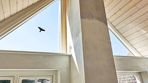 A building's interior with a large window and a bird flying outside.
