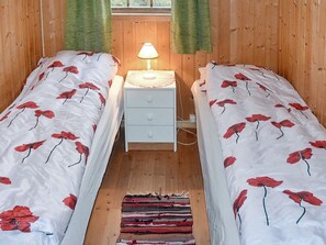 Una habitación con dos camas, una mesita de noche con una lámpara y un tapete a rayas.