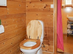 Un baño con paneles de madera, un asiento de inodoro de madera, un lavamanos blanco y un perchero rosa.