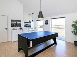 A room with a ping pong table, a dining area, and a large window.